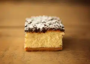 Zdjęcie przedstawia sernik wystawiony w witrynie Cukierni Śnieżka w Gorzowie Wielkopolskim. Jest sernik z pudrem. Wygląda apetycznie i domowo.